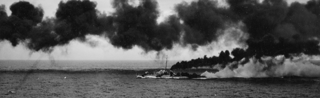 Dennis lays funnel (black) and chemical (white) smoke during the Battle off Samar, 25 October 1944, in this considerably enlarged image captured by a photographer on board the escort carrier Kitkun Bay (CVE-71). (U.S. Navy Photograph 80-G-287459,...