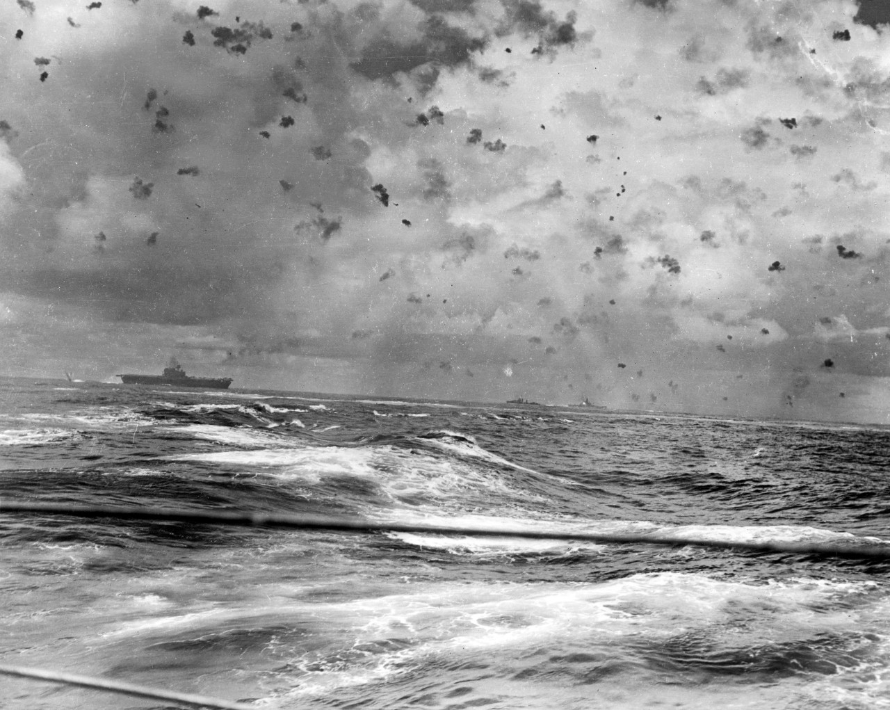 Antiaircraft gunners desperately fill the sky with flak and ships churn the water as they maneuver at speed and fight off the Japanese attackers, 26 October 1942. At least two enemy planes are visible above Enterprise, and the blast of South Dako...