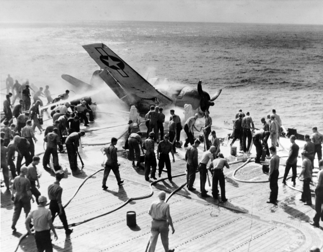 Flight deck crewmen extinguish the plane’s blaze, 10 November 1943. Johnson escapes without serious injuries, but sailors push the damaged Hellcat over the side and the ship continues toward the Gilberts. (U.S. Navy Photograph 80-G-205474, Nation...
