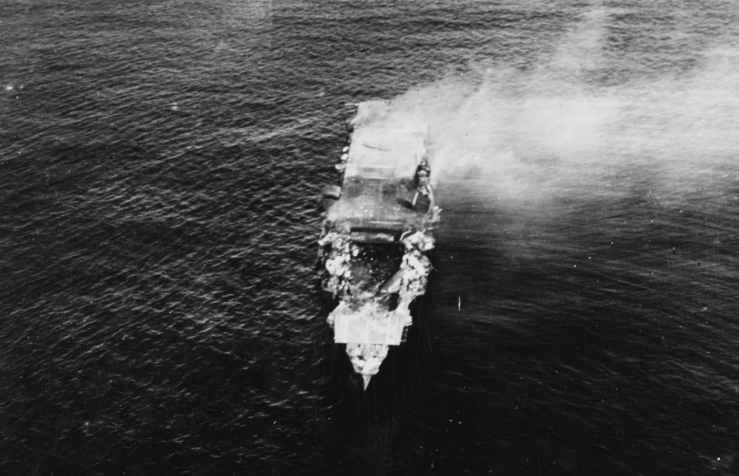 A plane flying from Hōshō takes this picture of Hiryū as she smolders shortly after sunrise, 5 June 1942. The exploding U.S. bombs have collapsed her flight deck over the forward hangar, and the ship will sink in a few hours. (Donated by Kazutosh...