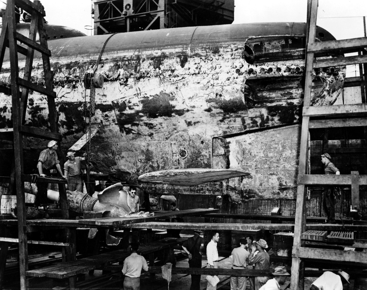 As Flier lies in dry dock at the Pearl Harbor Navy Yard, 31 January 1944, workmen contemplate the extensive damage received during the boat’s grounding at Midway earlier in the month. Note the broken port strut and the gnarled port screw. (U.S. N...