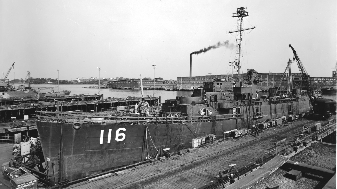 At the outfitting dock at the Bethlehem-Hingham yard, 5 July 1945, one month after launching. Note 5-inch/38 Mount 51 at high elevation, the gunhouse not yet being fitted, and a sister ship in the upper left background in what appears to be three...