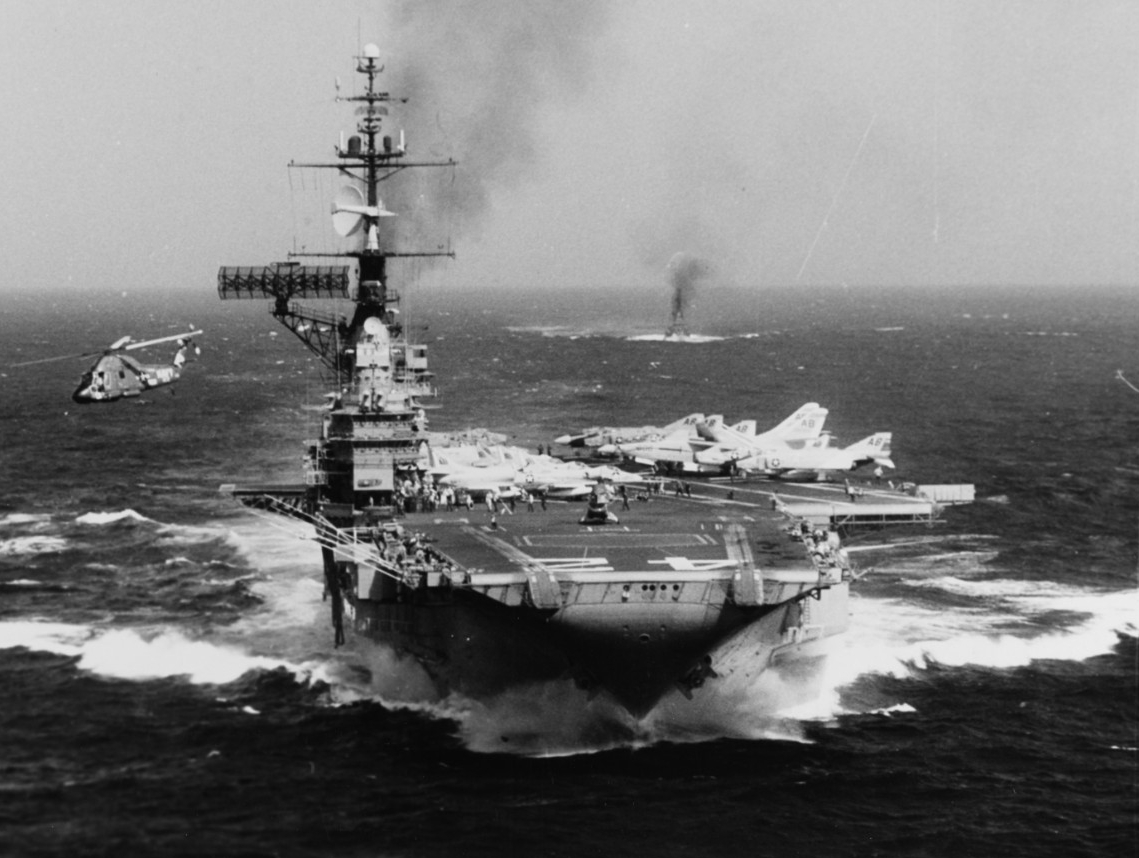 Franklin D. Roosevelt churns up the water as she steams in the South China Sea during the Vietnam War, 19 October 1966. One of her busy Seasprites lifts off and clears the ship to starboard, and the ubiquitous plane guard ship, a boon to pilots, ...