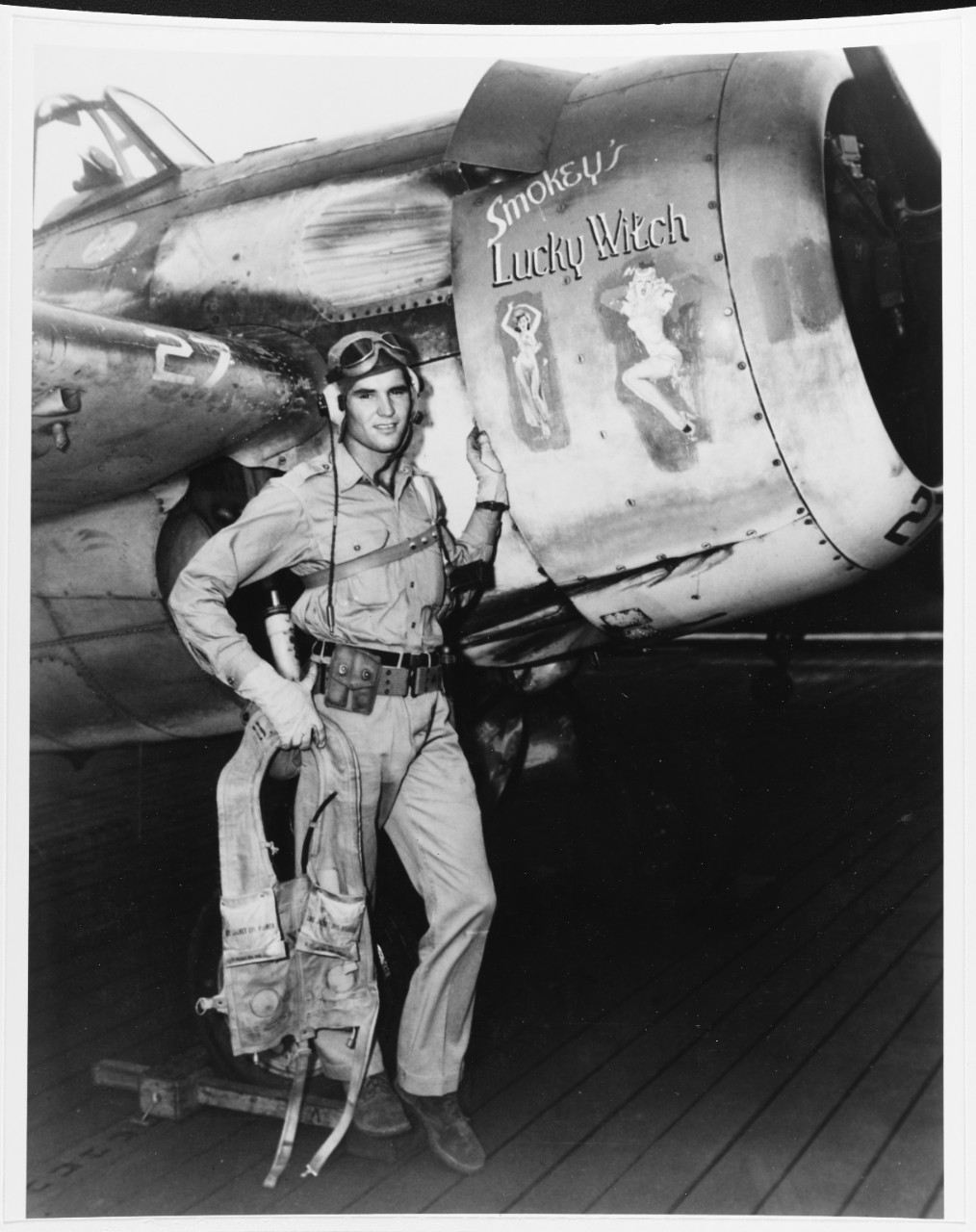 Ens. Darrell C. Bennett, USNR, stands beside “Smokey’s Lucky Witch”, his FM-2 Wildcat, on board Gambier Bay, 1 August 1944. Bennett strikes a jaunty pose carrying a Colt .45 cal. M1911A1 pistol in a shoulder holster as he leans on the fuselage an...