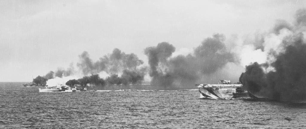 Gambier Bay (right) and two of her escorts, possibly Samuel B. Roberts (foreground) and Dennis (background), make smoke as the Japanese ships, faintly visible on the horizon, open fire at them, 25 October 1944. Photographed by PhoM1c Willard Neit...