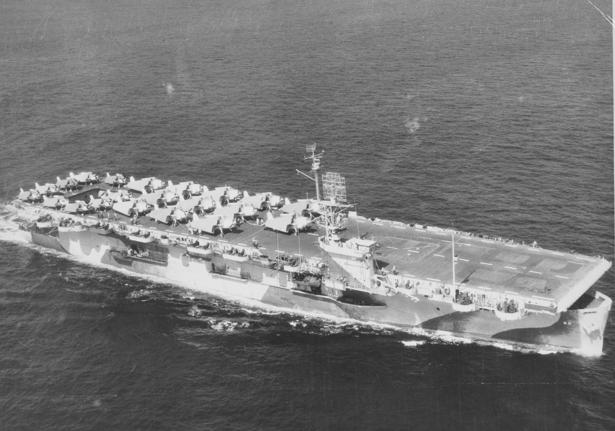 A K-type blimp of Blimp Squadron (ZP) 24 photographs Guadalcanal while the ship steams off Hampton Roads, 28 September 1944. All nine Wildcats and 12 Avengers are parked on the flight deck, amply demonstrating the limited room on board the carrie...