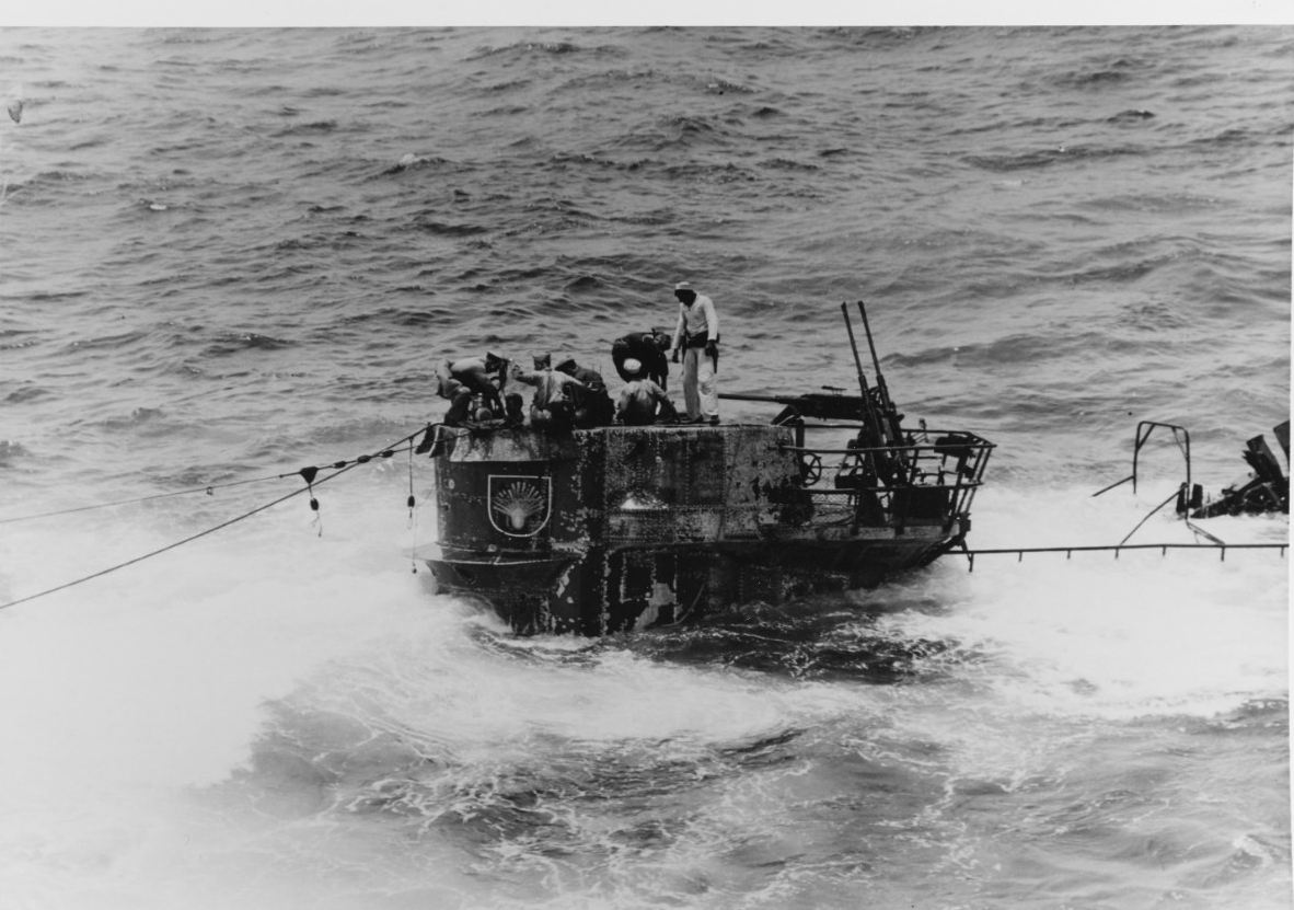 Men of the salvage party use a small handy-billy pump to dewater the boat. U-505’s freeboard is dangerously low as she settles, with only some of her fairwater above the surface. Note the twin 20 millimeter guns, and the seashell insignia on the ...