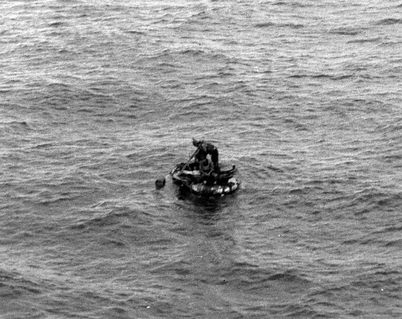 As first seen from Helm’s bridge on 17 May 1942, one of the four survivors on a raft from the sunken oiler Neosho stands to attract attention. (U.S. Navy Photograph 80-G-32131, National Archives and Records Administration, Still Pictures Division...