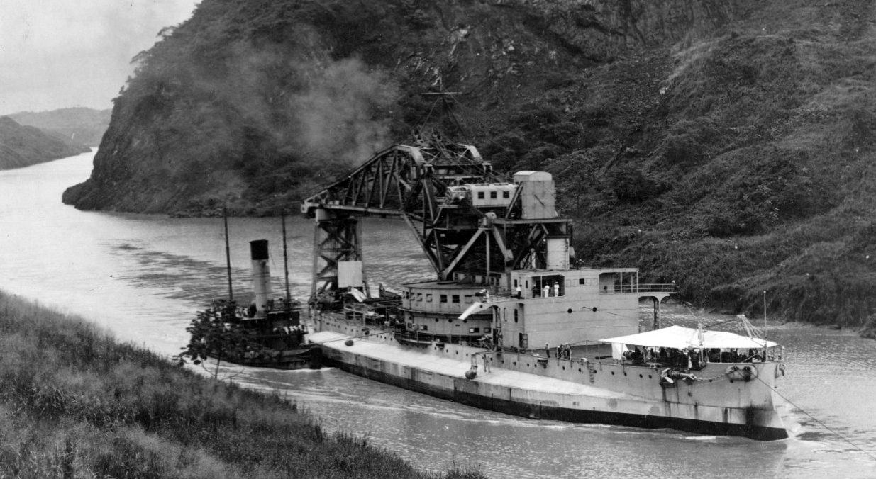 Crane Ship No. 1 passes through the Gaillard Cut of the Panama Canal, most likely during her shift between the coasts, 15 June–21 August 1926. Note the awning spread forward to protect her men from the scorching tropical sun. (Naval History and H...