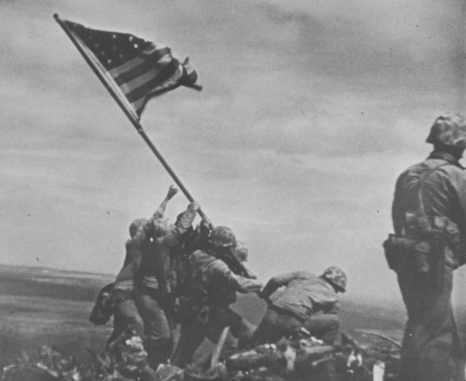 Marines raise the colors obtained from LST-779 on the summit of Mount Suribachi in this image captured on 16 millimeter motion picture film by SSgt. William H. Genaust, USMC, on 23 February 1945. (U.S. Marine Corps Photograph RG-127-GW-319-113057, National Archives and Records Administration, Still Pictures Branch, College Park, Md.)
