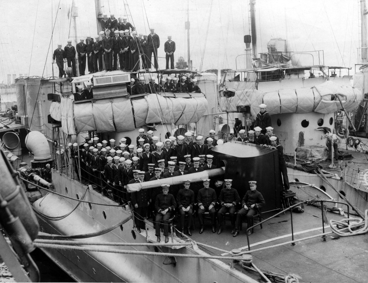 McDougal’s ship’s company arrayed for a group photograph, officers in the foreground, with chief petty officers immediately behind them. Note the shield on the forward gun and the framework to prevent the depression of the gun to fire into the fo...