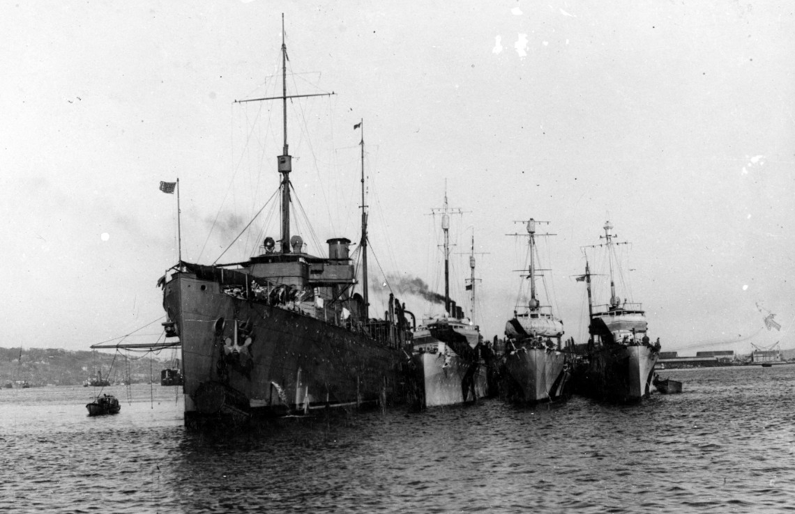 Melville lies at Queenstown, Ireland, with a trio of destroyers alongside in 1918, when British First Sea Lord Adm. Sir Rosslyn E. Wemyss, RN, visits the U.S. ships. The ships are painted in the wartime dazzle scheme but Melville’s is faded, mute...