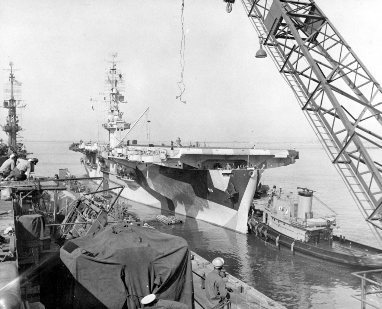 Midway, painted in a three-color disruptive camouflage, backs out of her berth at the Naval Repair Base, San Diego, following an availability there, assisted by harbor tugs, as seen from her sister ship White Plains (CVE-66), 10 April 1944. (U.S....