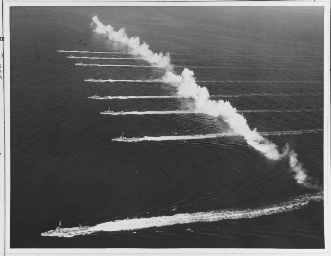 Ships of Destroyer Squadron (DesRon) 20 steam through a smokescreen laid by Consolidated P2Y-3s and Martin PM-1s of Patrol Squadrons (VPs) 7F, 9F, and 11F, during an exhibition staged for Movietone News off San Diego, Calif., 14 September 1936. The ships, from bottom to top are: Farragut (DD-348); Dewey (DD-349); Hull (DD-350); Macdonough (DD-351); Worden (DD-352); Dale (DD-353); Monaghan (DD-354) and Aylwin (DD-355). (Courtesy Cmdr. Robert L. Ghormley Jr., 1969, Naval History and Heritage Command Photograph NH 67293)