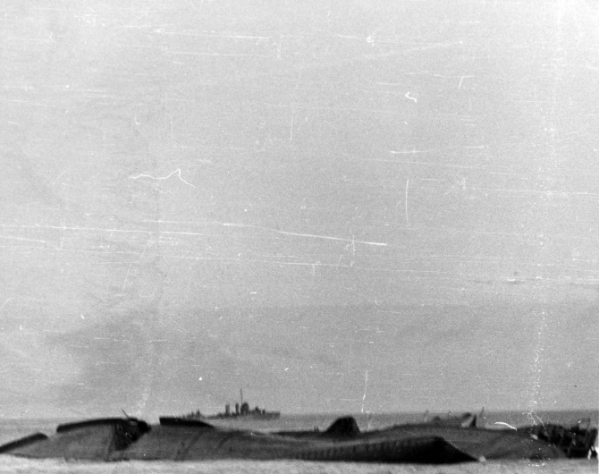 Yorktown sinks, as seen from an accompanying destroyer, just after dawn, 7 June 1942. Monaghan is in the left center distance. The carrier capsizes to port, exposing the turn of her starboard bilge. This view looks toward the ship’s bottom from off her bow, with Yorktown’s forefoot in the right foreground and her starboard forward 5-inch gun gallery beyond. The large hole made by one or two submarine torpedoes, severing the ship’s forward bilge keel, is toward the left. (Naval History and Heritage Command Photograph NH 106003)