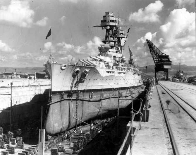 Nevada in Dry Dock No. 1 at the Pearl Harbor Navy Yard. Note the men painting her boot topping from stages rigged over the side, and the outline of her anti-torpedo blister where it merges with her forward hull. (Naval History and Heritage Command Photograph NH 50102)