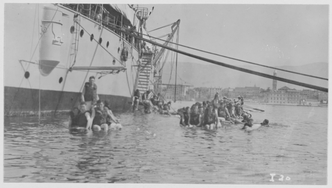 Men of the ships company swim alongside their cruiser in the Adriatic at Spalato. (R.E. Wayne I-20, undated U.S. Navy Photograph NH 122997, Photographic Section, Naval History and Heritage Command)