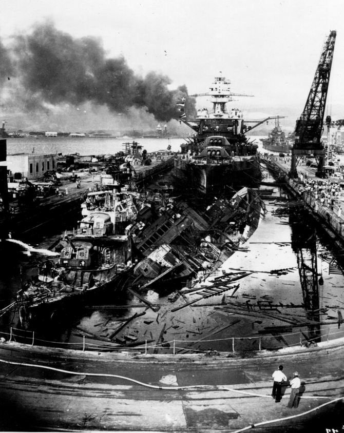 The wrecked destroyers Downes (DD-375) and Cassin (DD-372) in Dry Dock No. 1 at the Pearl Harbor Navy Yard, soon after the end of the Japanese air attack. Cassin has rolled off her blocks onto her sistership Downes. Pennsylvania lies astern, occupying the rest of the dry dock. The torpedo-damaged cruiser Helena (CL-50) is in the right distance, beyond the crane. Visible in the center distance lies the capsized Oklahoma (BB-37), with Maryland (BB-46) alongside. Smoke is from the sunken and burning Arizona (BB-39), out of view behind Pennsylvania. California (BB-44) is partially visible at the extreme left. This image has been attributed to Photographer's Mate Harold Fawcett. (U.S. Navy Photograph 80-G-19943, National Archives and Records Administration, Still Pictures Division, College Park, Md.)
