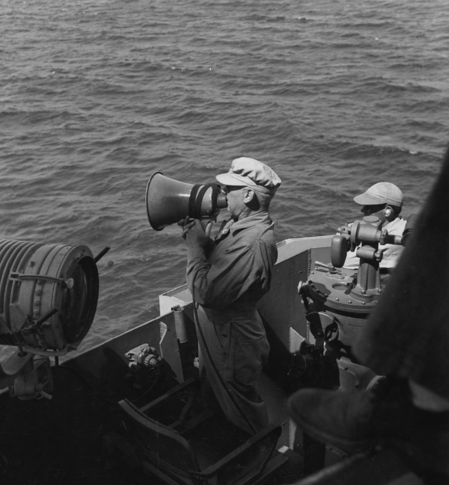Rear Adm. Berkey speaks to another ship via electric megaphone (or loud hailer) from the bridge of his flagship, Phoenix, as the Allied vessels shell Corregidor, 15 February 1945. The original caption identifies the ship as Australia, but she doe...
