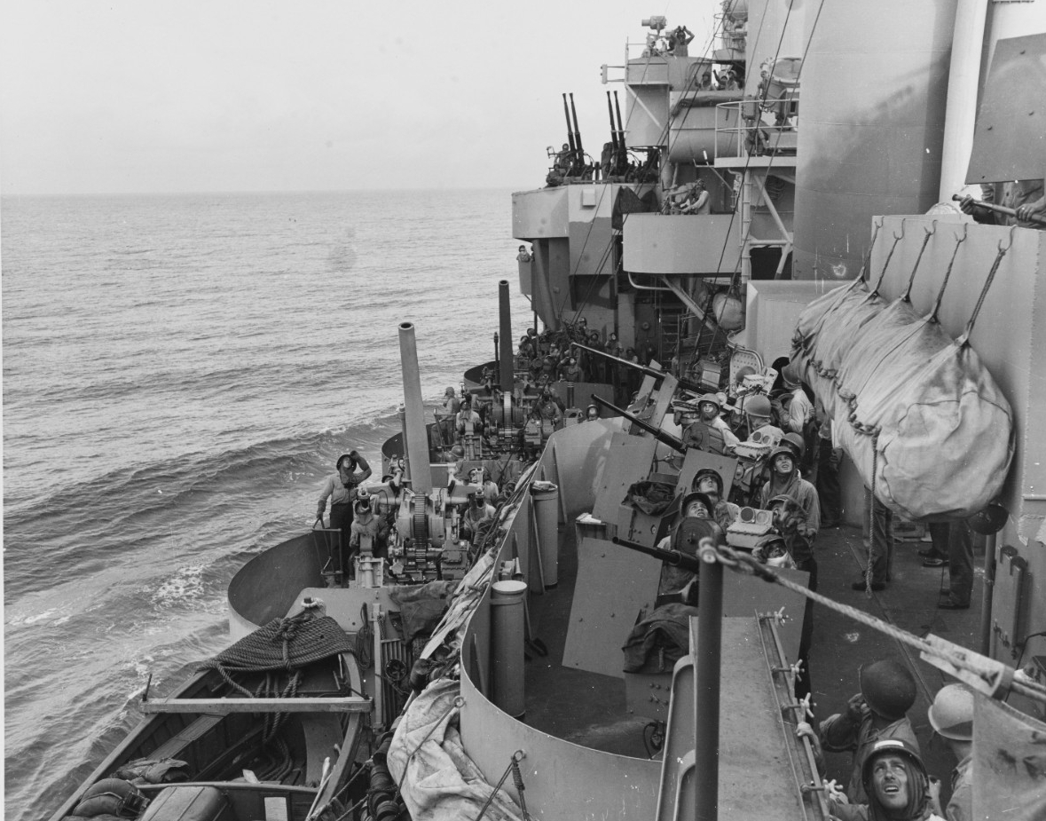 Men manning Phoenix’s port side 20 and 40-millimeter guns display the strain of the kamikaze attacks as they look skyward to identify a plane flying overhead while the ship steams to Mindor, 18 December 1944. Note the whaleboat in the lower left,...