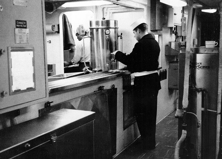 A crewman draws a cup of coffee in the ship’s mess decks, circa 1967. The sailor wears his coat and belt and is most likely standing a quarterdeck watch, which means that the ship lies moored. (Naval History and Heritage Command Photograph NH 75559)