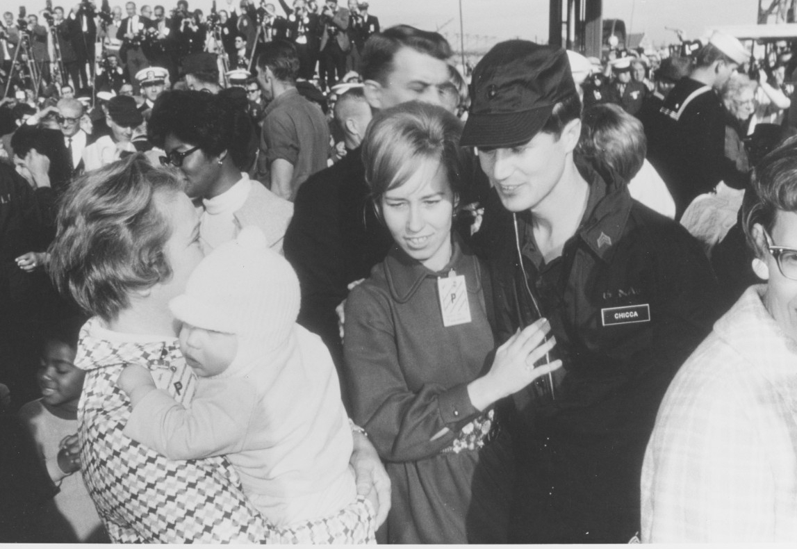 Sgt. Chicca greets his wife, Ann Marie, when the men return home to NAS Miramar on Christmas Eve 1968. Loved ones joyfully and tearfully reunite with the men following their ordeal, and an entourage of journalists film and photograph their homeco...