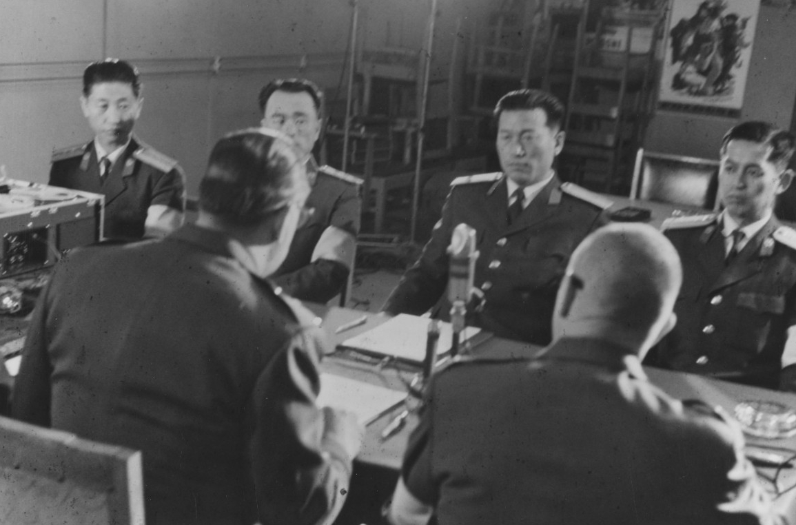American and North Korean representatives meet at Panmunjom to sign the agreement releasing the men, 22 December 1968. Maj. Gen. Woodward is seated in the left foreground, with his back to the camera. (Naval History and Heritage Command Photograp...