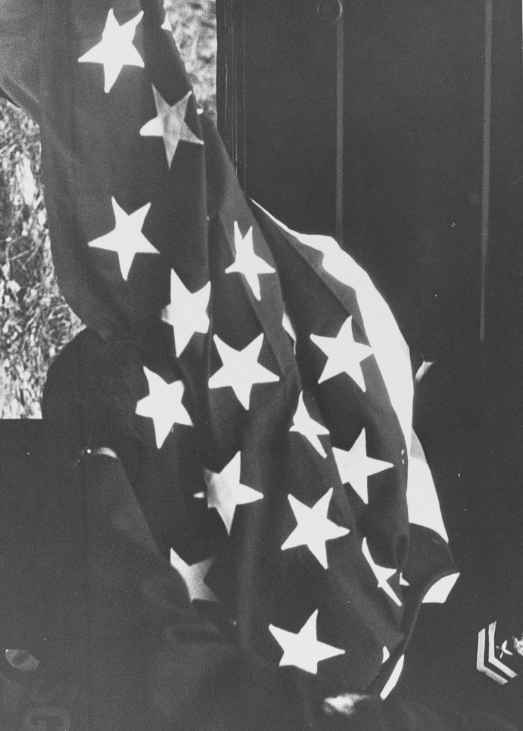 A Navy YN2 holds the U.S. flag that drapes Hodges’ coffin when his body returns to the United States, 23 December 1968. (Naval History and Heritage Command Photograph K-64690)