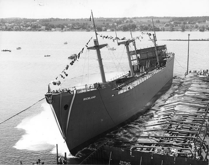 Reflecting the side-launching practice dictated by shipbuilding on inland waterways, Richland, her name in white block letters on her bow, enters her element on 5 August 1944, while the christening party watches her progress from the platform at lower right and spectators afloat and ashore look on. (U.S. Navy Photograph 80-G-266885, National Archives and Records Administration, Still Pictures Branch, College Park, Md.).