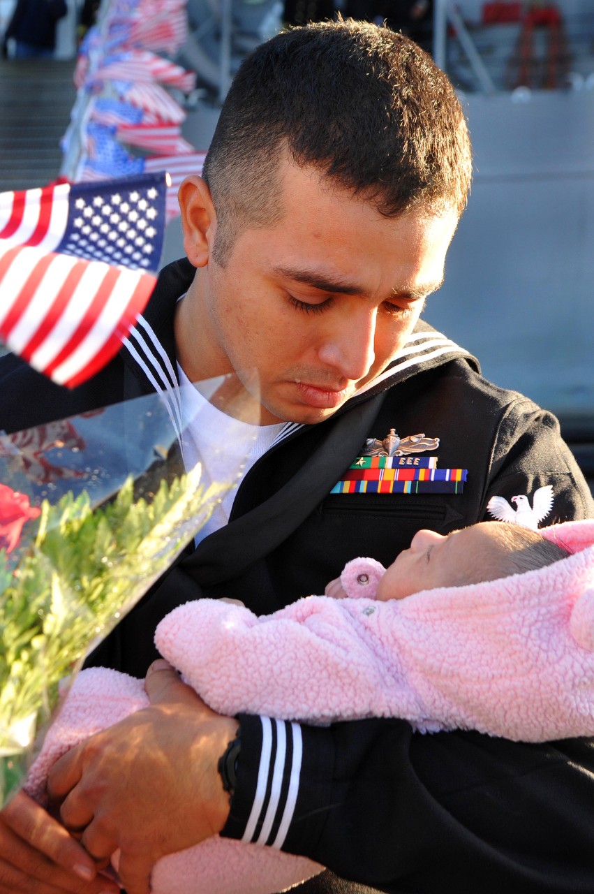 EN2 Stuardo Juarez greets his newborn daughter for the first time when he returns with the ship, 14 December 2011. (MC2 Jacob Sippel, U.S. Navy Photograph 111214-N-AW702-004, Navy NewsStand)