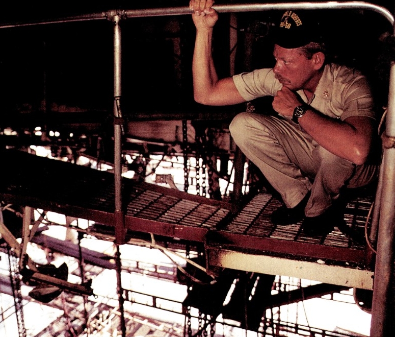 One of the ship’s crewmen reflects about the crew’s ordeal as he surveys the repair work at Dubai. (PH1 Chuck Mussi, All Hands, August 1988, No. 857, page 15)