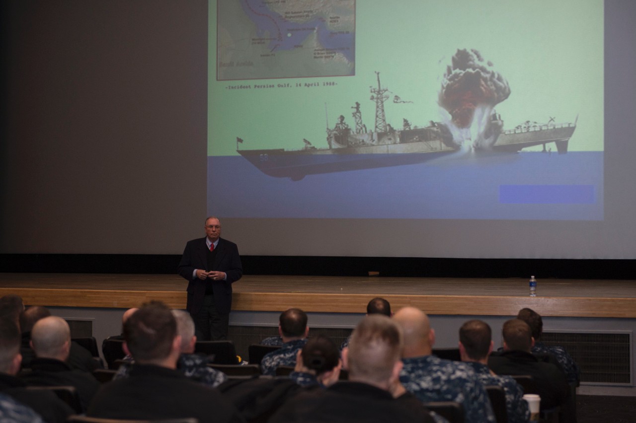 Capt. Rinn (retired) shares his experiences to junior officers during a Surface Warfare Junior Officer Tactical Program summit at Fleet Activities Yokosuka, Japan, 9 February 2015. The image on the screen aptly demonstrates the mine’s devastating...