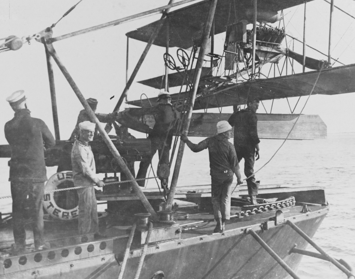 Curtiss AH-12 seaplane on the hoist of Sterett, circa 1915. Note the steering chain running along Sterett's deck. (Naval History and Heritage Command Photograph, NH 2246)