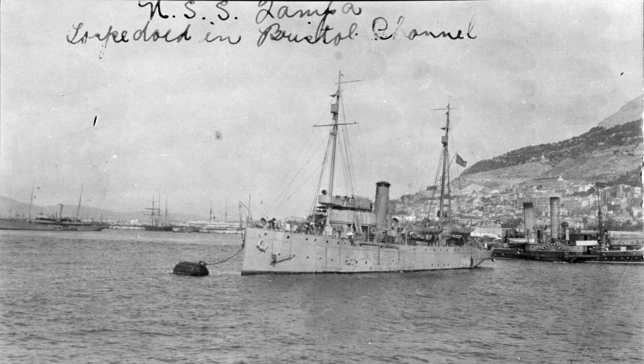 Tampa moors in a European port (possibly Gibraltar), during World War I. The original image is printed on post card stock. Note the paddle tug astern of Tampa and the large converted yacht in the left distance. The latter may be a British Navy ve...