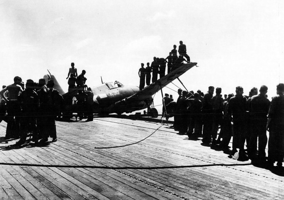 White Plains accomplishes her first carrier landings, including this fighter that makes an off-center landing on the flight deck, 16 January 1944. Sailors struggle to handle the plane out of its precarious position, and some of the men stand on i...