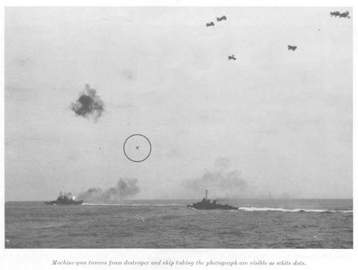 Japanese fighter plant ("Zeke") continuing the dive on cruiser. Flame and smoke from cruiser caused by firing of AA batteries. Machine-gun tracers from destroyer and ship taking the photograph are visible as white dots.