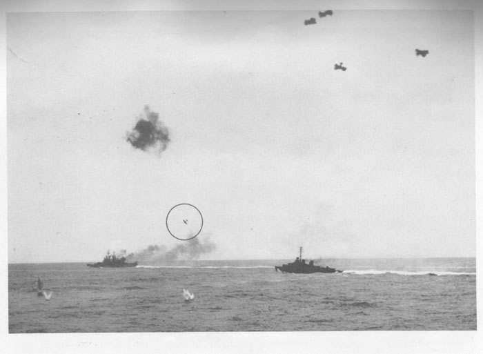Japanese fighter plane ("Zeke") continuing dive on cruiser which is trailing smoke from fire of her own AA batteries.