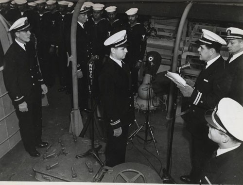 "'Subchaser manned by Negroes is commissioned at New York, 25 April 1944.' Lieutenant Eric Purdon, USNR, reads the orders directing him to assume command of the USS PC-1264, as officers and men of the ship's company stand at attention. The 173 foot sub hunter joins the naval service with 53 Negroes in her crew."