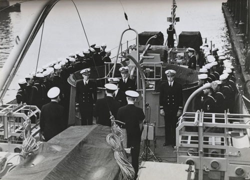 "'Subchaser manned by Negroes is commissioned at New York, 26 April 1944.' The national Ensign is raised on the USS PC-1264, and crew members stand at attention on the fantail as the commissioning ceremony is completed."
