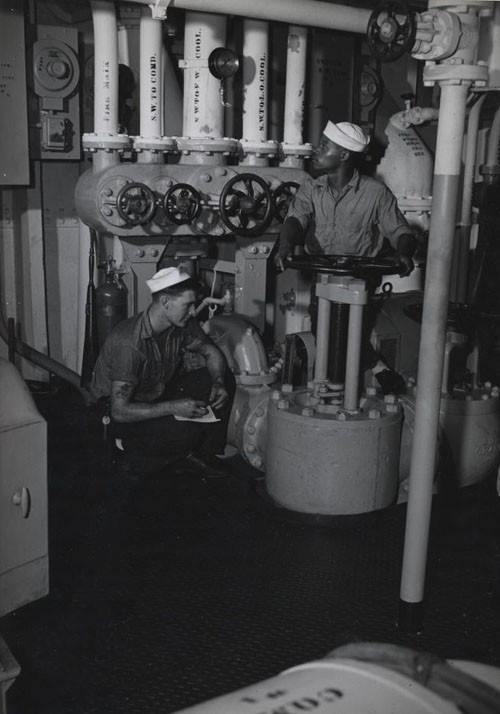 "Recording pressures in the engine room aboard this ship somewhere in the Pacific is Metalsmith Ben L. Dunn, Jr., while George Redd, Fireman Second Class, mans a valve as he keeps an eye on the gauge."