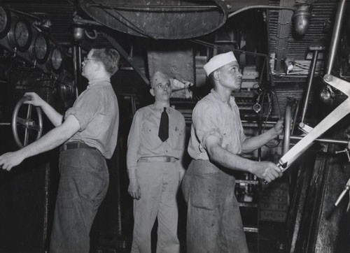 "Main engine throttles are handled aboard a large ship somewhere in the Pacific by Robert E. Beach, Machinist's Mate Second class, USNR, and Clarence Spears, Machinist's Mate Third Class, USNR. In the center is Chief Machinist's Gentry D. Keathley, Assistant engineering Officer. Machinist's Mate Spears stood third in his class at the machinist mate service school at Great Lakes, Illinois, and is doing an exceptionally good job aboard this ship according to Chief Keathley."