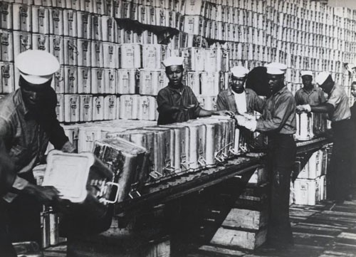 "Navy Negroes 'Pass the Ammunition.' - More than 6,000 Negro enlisted men are now serving in the Navy's ordnance station, performing their duties with an ability and zest which has qualified many for promotion. These youths passing 1.1 shell cans down a conveyor for stacking are assigned to St. Juliens Creek Naval Ammunition Depot. The duties that may be assigned to these enlisted men range from manual tasks to handling 'live' ammunition at the battlefronts. A number of the most skilled have been already sent overseas, and more will be sent out as replacement recruits fill the ranks at US bases."