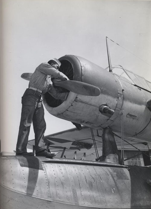 "Working on the motor of an OS-2-V, at US Naval Air Station, Seattle, Washington."