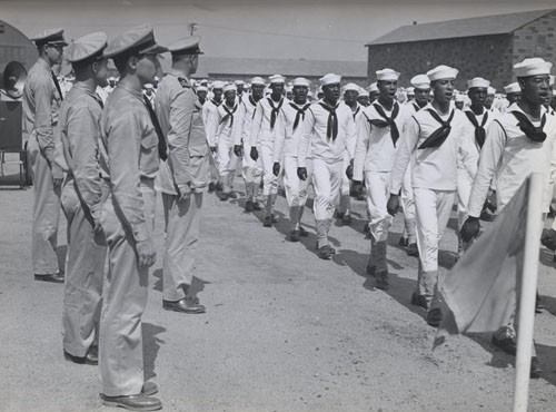 "A company of Negro recruits sing one of its own marching songs as it passes Lieutenant Commander Daniel W. Armstrong, commanding officer of Camp Robert Smalls, and his staff during a military review."