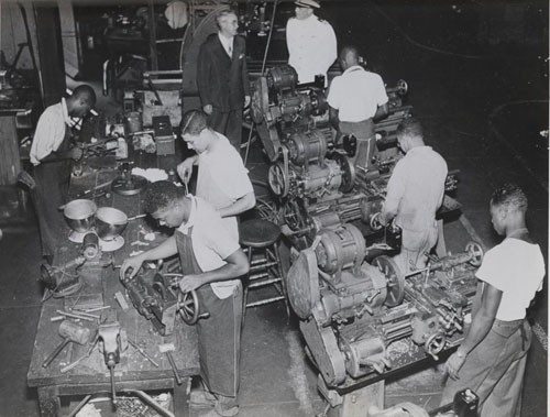 "Machine Shop at Hampton Institute, Virginia. Dr. Malcolm S. MacLean, president, and Lieutenant Commander E.H. Downes, USN (Ret.), watch regular students of the Institute at work."