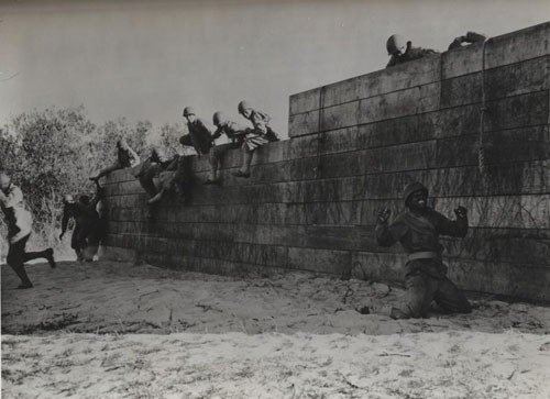 "'Up and at 'em' - Undergoing a stiff training course in order to get in trim for stern duties ahead, Negro Seabees hurdle a high fence as one feature of a trying obstacle course. One of them came down on his knees - but by the wide grin he wears, he is unhurt, will soon be up and off."