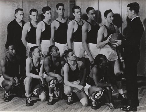 "Chief Specialist John J. Gilmartin is shown giving members of his US Naval Hospital basketball team last minute instruction before a game. Back row, (left to right), Werling, Sinager, Morin, Wilson, Fairchild, Fouse, Johnson. Front row (left to right), Pickett, Anderson, Thomas, Duff, Williams, and Coach Gilmartin."