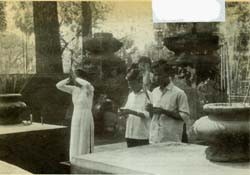 Common Vietnamese gesture of worship, the "lay" (pronounced "lie") is performed by woman at left with joss sticks in clasped hands.