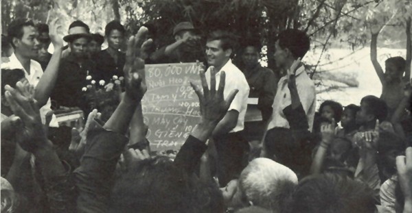 Image - South Vietnamese villagers vote on the use of the community development budget of 80,000 piasters allocated by the provincial administration. An AID field representative holds a blackboard listing the items voted on. They include pig raising, health station, schoolhouses, tractors, wells, and buffaloes. 