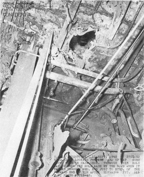 Photo E-3: First hit. Looking aft and upward from compartment D-203-1LM through bomb passage hole in main deck to bomb passage hole in bulkhead 173 between the main and gallery decks.